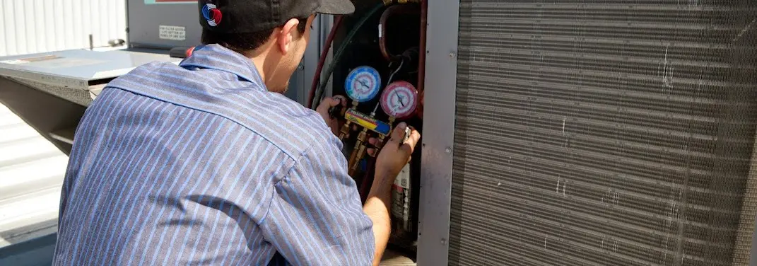 HVAC technician servicing a condenser unit in Manor